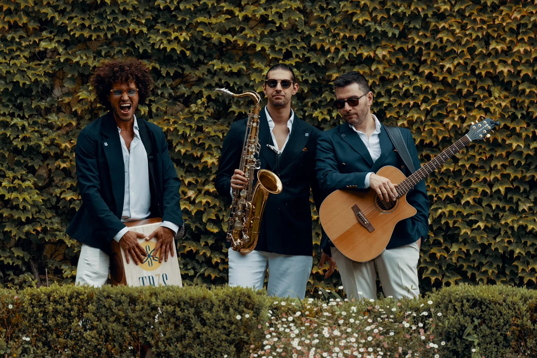 The three musicians in navy blazers laughing together in front of an ivy wall