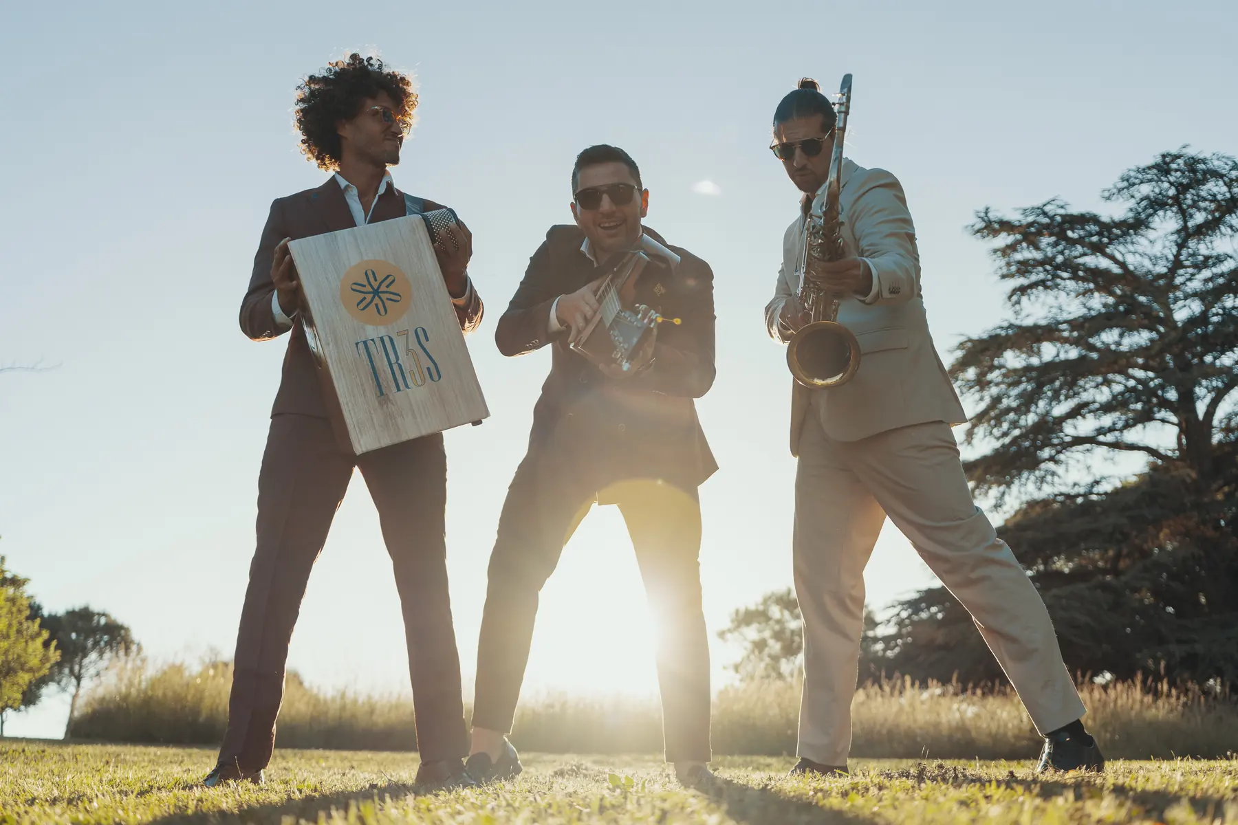 TR3S dancing with their instruments against a clear sky, the sun low between them