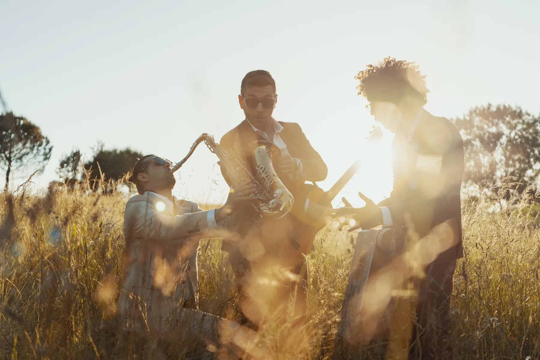 TR3S playing together in a field of tall golden grass with the sun flaring behind them